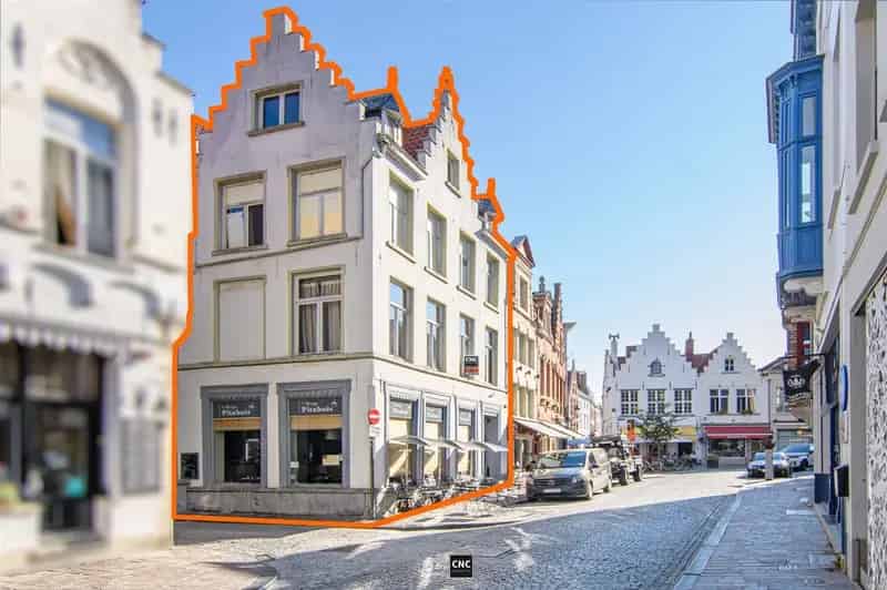 Handelspand met woonst op een commerciële en toeristische goede ligging, op wandelafstand van de Grote Markt en de Burg, in de schaduw van het Belfort, Het Provinciaal Hof en het stadhuis, met brede gevel en goede zichtbaarheid door zijn hoekligging.